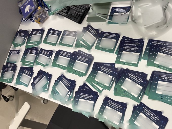 Numerous blue and green name badges and 'Tournament Night' cards spread across a table for a Tokenizing AI & Pop Charity Night event.
