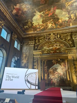 An ornate Baroque interior with elaborate ceiling frescoes, where a display board reads 'The World is Flat' against the gilded architectural backdrop.