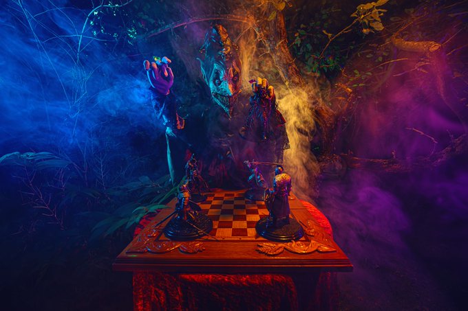 A dramatic, fantasy-themed still life featuring chess pieces on a wooden board illuminated by blue and purple lighting, with a large menacing king piece looming in a smoky, mystical forest setting.