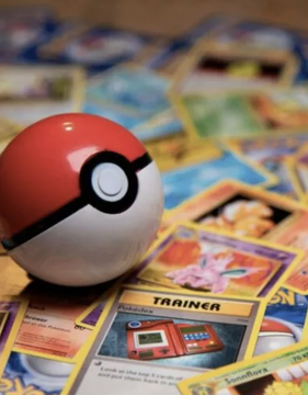 A Poké Ball sitting on top of a spread of Pokémon trading cards, with a 'TRAINER' card visible beneath it.
