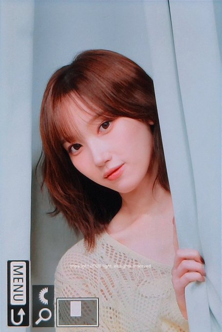 A close-up portrait of a young woman with brown hair peeking out from behind a light blue curtain, with UI elements and text reading 'copyright ©nbc light. all rights reserved' visible at the bottom.