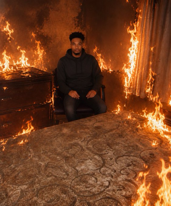 The image features a man sitting in a chair, surrounded by flames that are burning through a room. The fire appears to be consuming everything within its reach, including furniture like chairs and beds. The scene takes place in front of a dresser with a drawer open, adding to the intensity of the situation. The caption for this image includes a meme about Fine, which is related to USDC and pumpfun shilling, suggesting that the post might be promoting a charity or fundraiser.