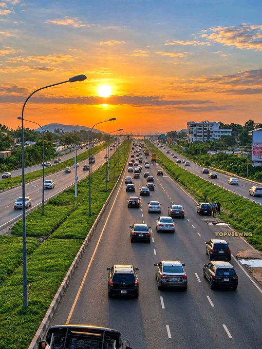 An aerial sunset view of a busy multi-lane highway filled with traffic, set against a vibrant orange and blue sky.
