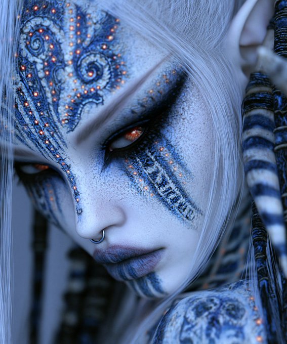 A striking close-up portrait of a pale-skinned figure with flowing white hair, adorned in elaborate blue and orange intricate body art and makeup, featuring glowing orange eyes and a silver nose ring. The image's dominant blue tones and ornate patterns visually echo the "something Blue" theme mentioned in the post.