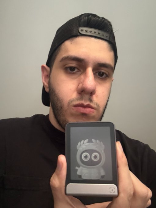 A selfie of a bearded man wearing a backwards black cap, holding up a small device displaying the 3D scan of a Kenny from South Park figure.