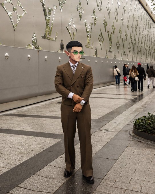 A stylish man in a brown double-breasted suit and green-tinted sunglasses stands confidently on a patterned walkway beside a decorative metallic wall, exuding a polished, ready-for-business vibe. The image pairs with the morning greeting as a visual embodiment of stepping into the day poised for success and productivity.