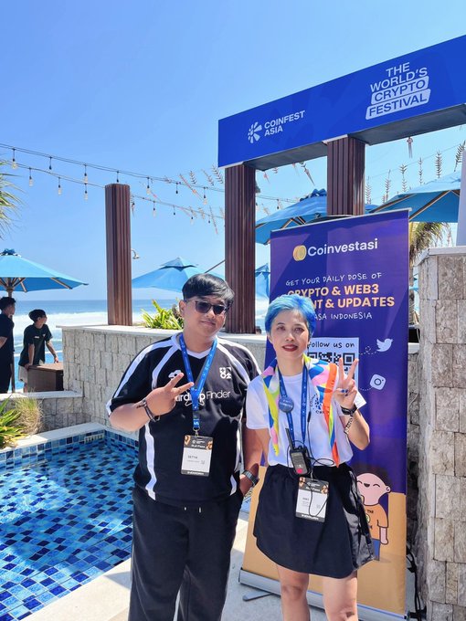 Two people pose at the Coinfest Asia event, which is advertised as "The World's Crypto Festival," standing in front of a Coinvestasi banner promoting crypto news and updates in Indonesia.