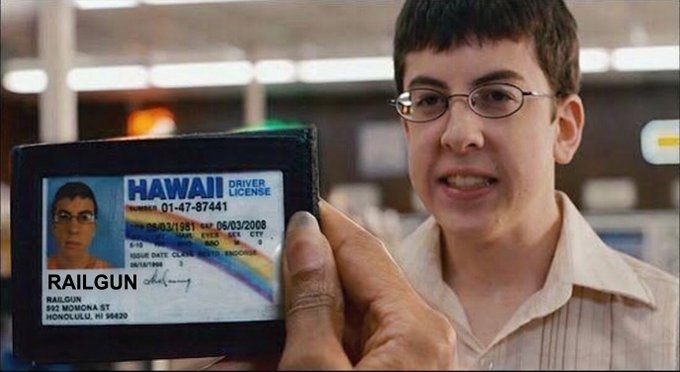 The image shows a young man holding up his driver's license, which has Hawaiian writing on it. This suggests that he might be from or have an interest in Hawaii. The photo also includes text that reads "Gm @RAILGUN_Project $RAIL". This could indicate that the person is involved with a project related to the "RAILgun" brand or has some connection to the Hawaiian theme of the driver's license.