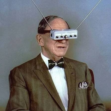 A retro television advertisement photo shows an older gentleman in a tweed suit and bow tie wearing a strange head-mounted antenna device with two prongs extending upward.