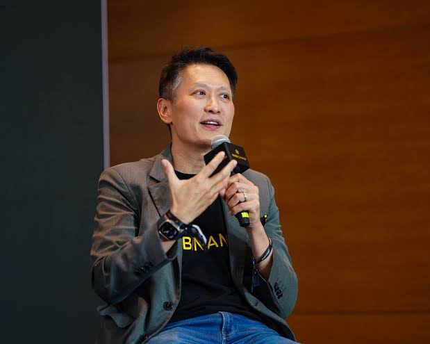 A man in a gray blazer over a black t-shirt featuring "BINAN" text speaks into a Binance-branded microphone, appearing engaged in a public speaking event. The image aligns with the accompanying post, depicting Binance CEO Richard Teng discussing tokenisation and accessibility in private markets.