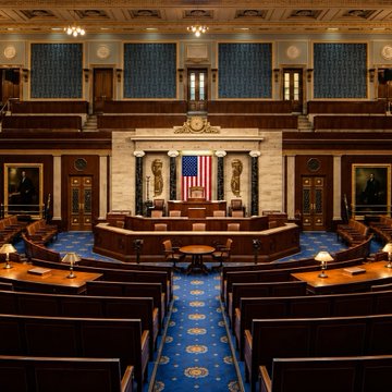 An empty Senate chamber inside the U.S. Capitol, featuring a central podium, the American flag, and rows of unoccupied desks arranged on a blue carpet, with no visible text or numbers, symbolically representing the recent failed CLARITY Act vote as senators are absent from the floor.