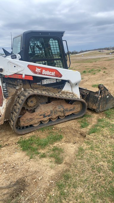 A muddy Bobcat skid-steer loader parked on a grassy dirt field under an overcast sky.