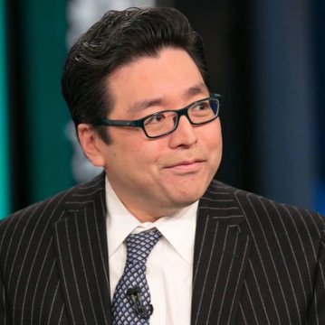 A man with dark hair and black glasses wearing a dark pinstripe suit, white shirt, and patterned tie.