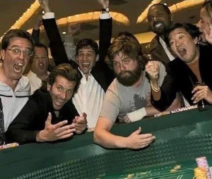 An iconic celebratory photo showing a group of excited men cheering at a casino craps table, with Bradley Cooper, Zach Galifianakis, and others raising their arms in victory.