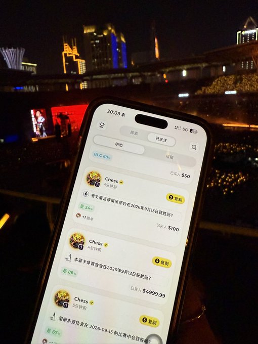 A hand holds a smartphone displaying the Chess.xyz prediction market app at 20:09 with 5G connection, showing bets like "孝文易足球俱乐部会在2026年9月13日获胜吗？" at $100 and 本菲卡 vs 里奥本体育会 matches, as the user finds signal to copy-trade during a concert, attempting to recover losses from the previous night under the illuminated night skyline.