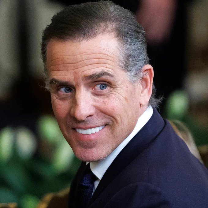 A close-up portrait of an older man with gray hair, wearing a dark suit jacket, white shirt, and dark tie, smiling at the camera.