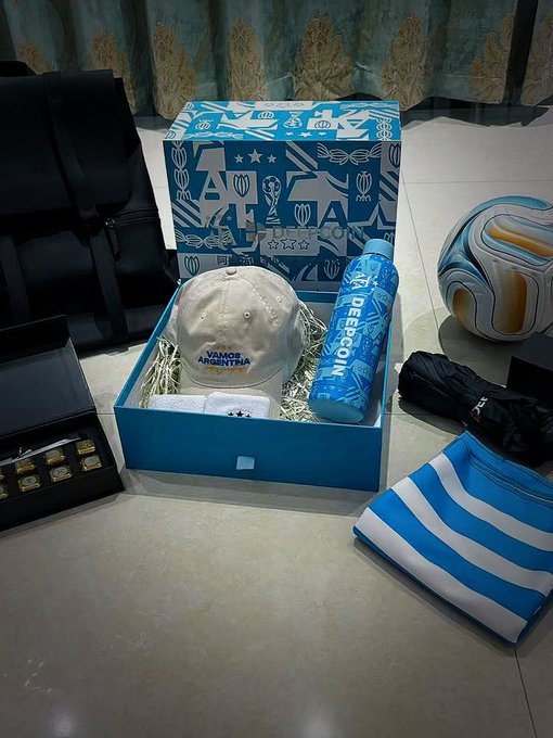 A blue World Cup-themed gift box containing Vamos Argentina merchandise including a cap, Deeroon water bottle, ball, and other items.