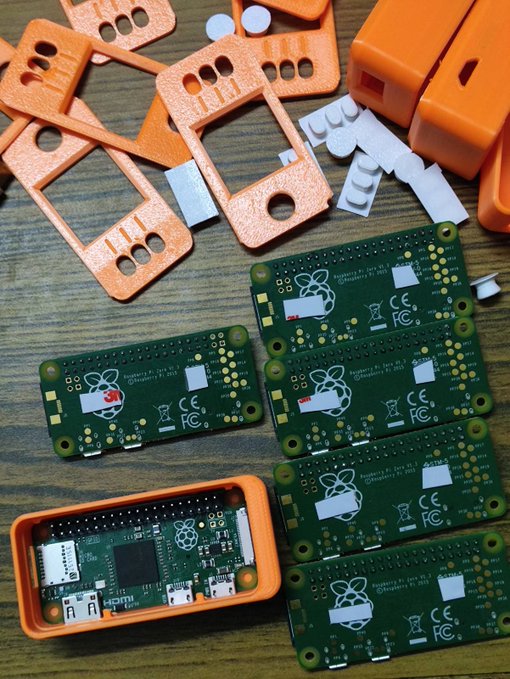 Several Raspberry Pi Zero circuit boards (labeled "Raspberry Pi Zero v1.3" and "Raspberry Pi Zero v1.2") are shown alongside 3D-printed orange case components and mounting hardware, with one Pi Zero assembled into its orange case—representing the core hardware of DIY SeedSigner Bitcoin signing devices being built en masse in India.