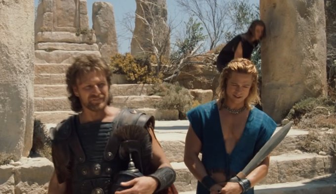 A scene from the 1982 film "Conan the Barbarian" showing Arnold Schwarzenegger with a sword standing next to a companion on stone steps.