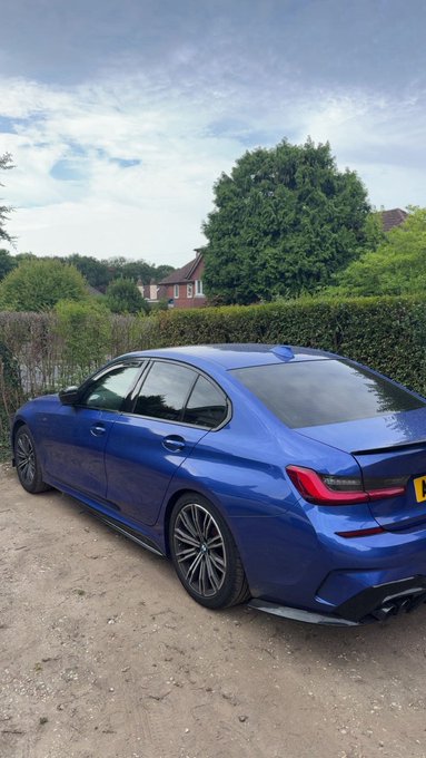 A vibrant blue BMW M3 sedan is parked on a dirt path, with "GM bros" likely referencing the car's iconic performance status and German engineering. The aggressive stance and quad exhaust tips suggest a high-performance variant, appealing to car enthusiasts.