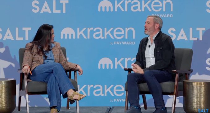 A panel discussion at a SALT and Kraken (by Payward) conference, featuring a woman in a plaid blazer speaking with a man in a dark jacket.