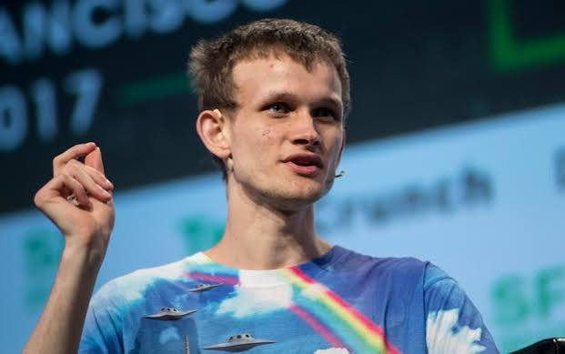 A photo of Vitalik Buterin, co-founder of Ethereum, speaking at an event while wearing a tie-dye shirt with UFO graphics.
