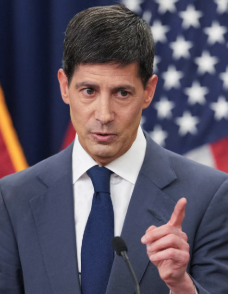 A dark-haired man in a blue suit and dark tie gestures with his finger while speaking at a podium, with American and Arizona state flags visible in the background. The image likely depicts a Federal Reserve official, contextualizing the post's discussion of the Fed maintaining hawkish monetary policy and the rising probability of multiple interest rate hikes extending into 2027.