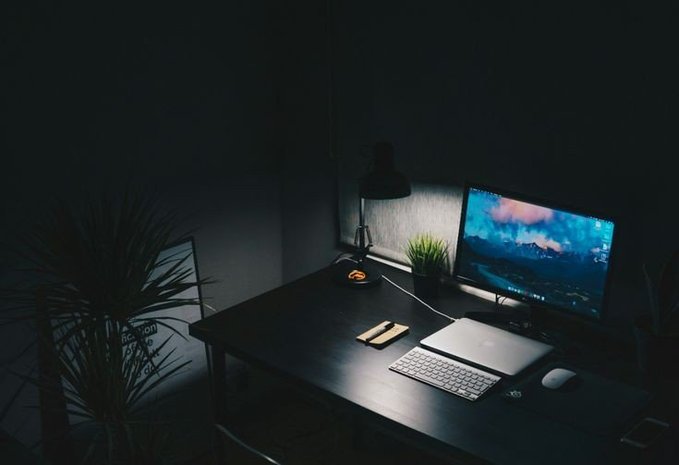 A dimly lit desk setup featuring a monitor displaying a scenic wallpaper, a keyboard, mouse, laptop, desk lamp, and a small potted plant. The image reflects the "locked in" mood of the caption, showing a quiet, focused workspace ready for an evening of studying and building, with @NucleusCodes tagged as the creator.