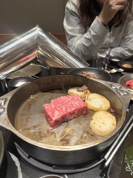 A thick, marbled cut of raw Wagyu beef sizzles alongside golden potato slices on a tabletop grill, with a partially visible diner in a white shirt across the table. The luxurious meal imagery visually underscores the celebratory, high-value tone of a crypto project listing announcement on Upbit Korea.