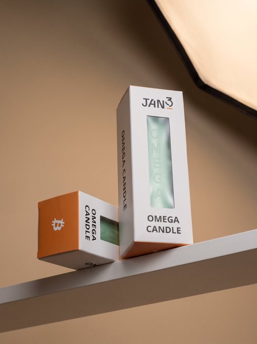 Two "Omega Candle" boxes from JAN3, branded with the orange ₿ Bitcoin logo, are displayed on a shelf—visually reinforcing the post's message that this peppermint essential oil candle is a must-have accessory for Bitcoin enthusiasts.