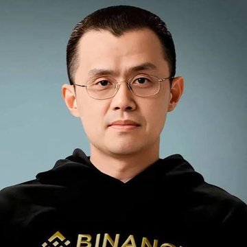 A portrait of Changpeng Zhao (CZ), founder of Binance, wearing glasses and a black hoodie with the Binance logo visible at the bottom.
