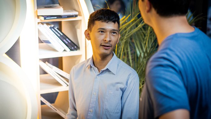Francisco (@Constant9Ghost) of the Bitcoin Office shows a German business delegation the Bitcoin Zone in Apopa, a space designed with the local community. The image captures a moment of conversation within the modern, well-lit Bitcoin Zone, highlighting its welcoming atmosphere.