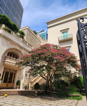 The image shows an elegant building in Seoul featuring a grand stone archway entrance, a flowing pink crepe myrtle tree in full bloom, and a modern high-rise rising in the background. This refined venue sets the perfect upscale stage for the WAVIST Night event, where discussions on tokenizing K-pop entertainment IP are about to unfold during KBW (Korea Blockchain Week).