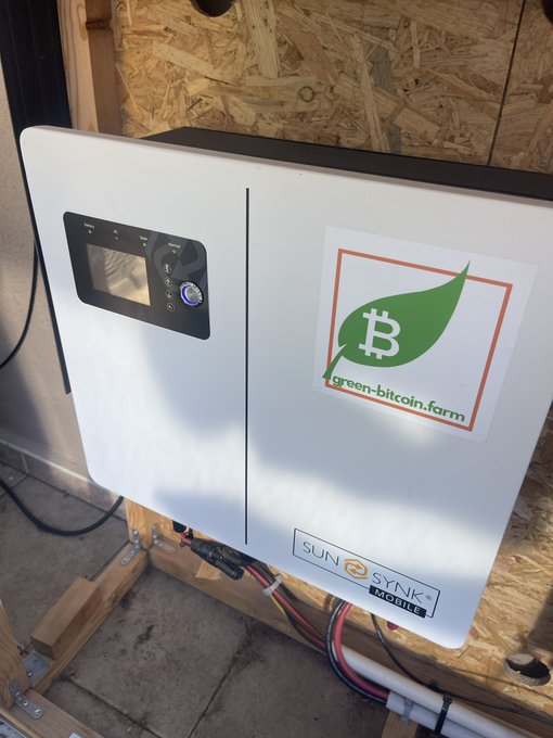 A Sunsynk Mobile solar inverter with a "green-bitcoin.farm" Bitcoin leaf logo sticker is mounted on an OSB wall, illustrating the article's point about using surplus solar energy for home Bitcoin mining amid Germany's new 100 kW feed-in restrictions.