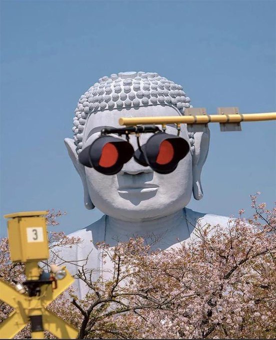 A massive white Buddha statue has been humorously edited to wear red and black sunglasses, with a railway signal labeled "3" in the foreground and cherry blossoms below. The "cool" sunnies play into the playful caption "Me on the @world_xyz website," suggesting the user is the laid-back Buddha browsing a virtual world.