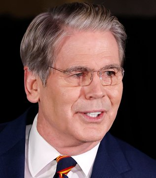 U.S. Treasury Secretary Scott Bessent, seen here in a navy suit with a striped tie and wire-frame glasses, is pictured as he publicly urges the Senate to pass the Clarity Act. The image accompanies breaking news of his push for the bill, which he deems essential for U.S. tech leadership while protecting community banks from stablecoin-related risks.