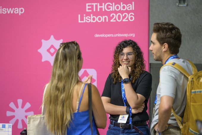 Three people converse at ETHGlobal Lisbon 2026, with a pink Uniswap-branded backdrop displaying 'developers.uniswap.org' visible behind them.