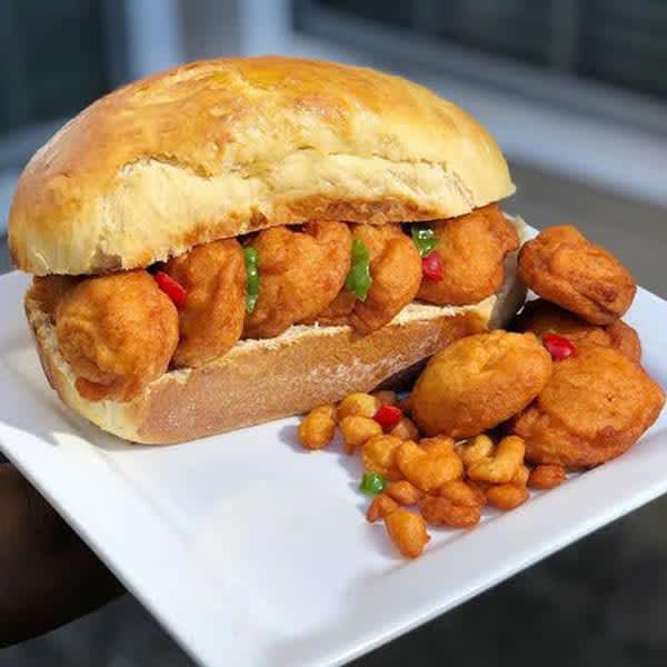 A close-up of a sandwich filled with fried chicken nuggets and diced red and green peppers on a white plate, accompanied by additional nuggets on the side.