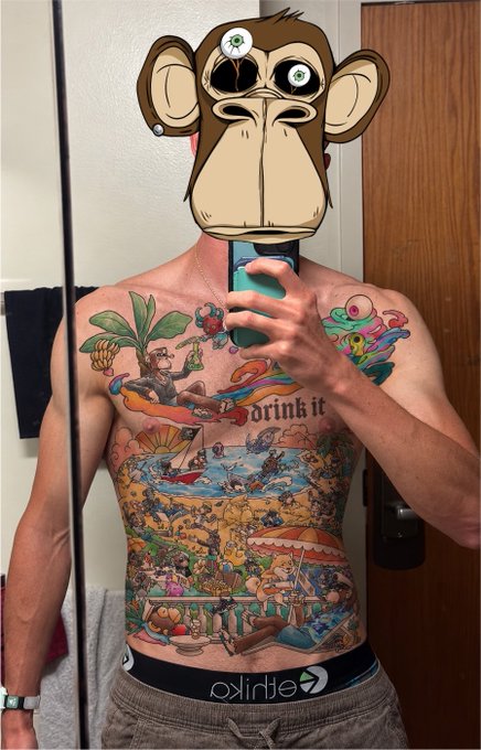 A shirtless man takes a mirror selfie, his face obscured by a cartoon monkey mask, showcasing an elaborate, colorful chest and stomach tattoo featuring a beach scene and the text 'Drink it', while wearing 'ethika' branded underwear.