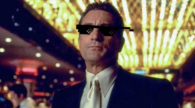 A man in a black suit and white tie stands in a casino with blurred lights in the background; pixelated "deal with it" sunglasses have been digitally added over his eyes.