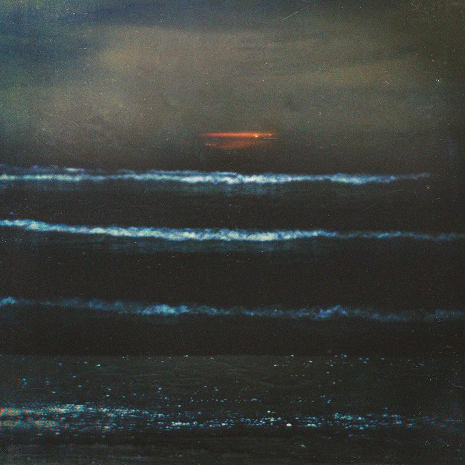 A dark, grainy atmospheric image showing layered horizontal cloud formations or mist with a reddish-orange glow near the top against a dark sky.