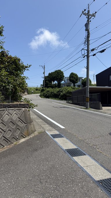 An empty street on a sunny day with blue sky, power lines, utility poles, and a few buildings along the roadside.