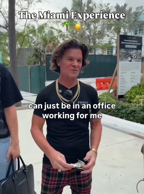 A man in a black t-shirt and plaid pants standing on a city street, overlaid with text reading 'The Miami Experience' and 'can just be in an office working for me,' with sunglasses hanging from his gold chain.