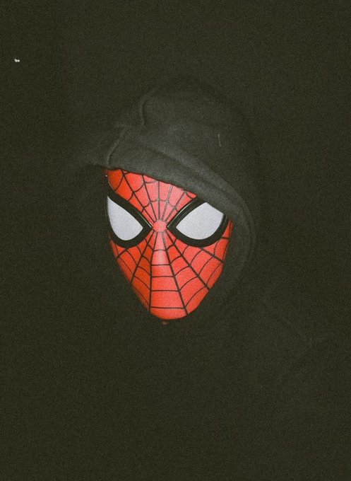A Spiderman-themed item, possibly a plush or small figure, peeking out from inside a dark hoodie against a black background.
