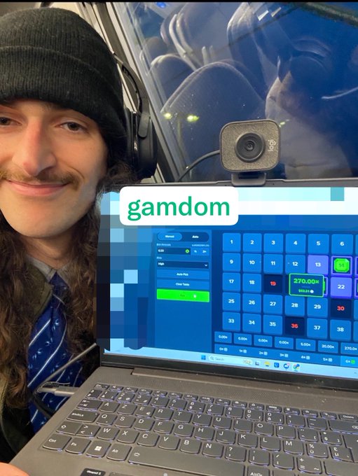 A man with a mustache and beanie smiles while using a laptop displaying the Gamdom betting site, where the "Crash" game shows a recent win of $270.00. The image humorously contrasts the post's nostalgic lament about $60 being enough for food and rent with the modern reality of online crypto gambling winnings.