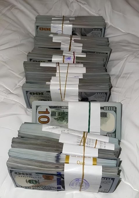 Multiple stacks of U.S. currency, including $10 and $100 bills, bundled with paper straps and rubber bands on a white surface.