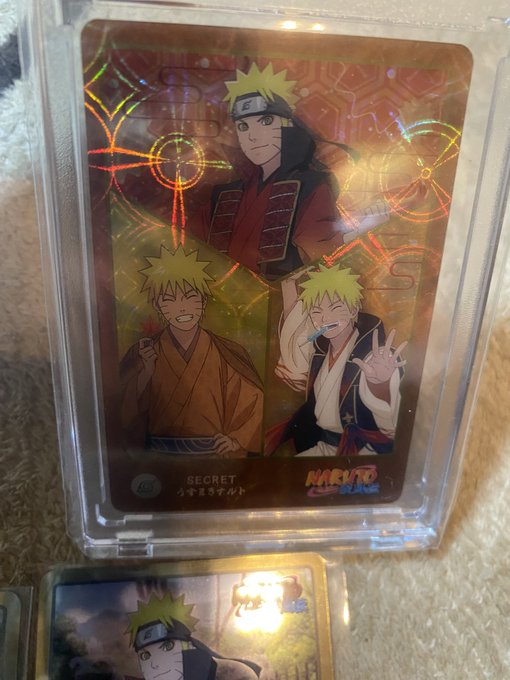A holographic "SECRET" Naruto trading card in a protective case showing three versions of Naruto Uzumaki, with Japanese text "うずまきナルト" and the Naruto Shippuden logo.
