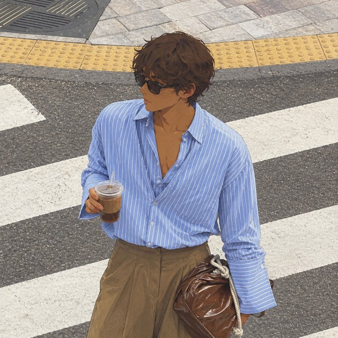 A stylish young man with tousled brown hair and sunglasses stands on a crosswalk, holding an iced coffee and a brown leather bag, dressed in an unbuttoned blue pinstripe shirt and khaki trousers—embodying a relaxed, sunny Saturday vibe.
