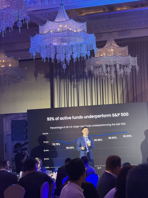 A presenter in a blue suit stands before a screen at a conference titled '93% of active funds underperform S&P 500,' showing a line graph with percentages ranging from 66.84% to 92.89% over 10 years.