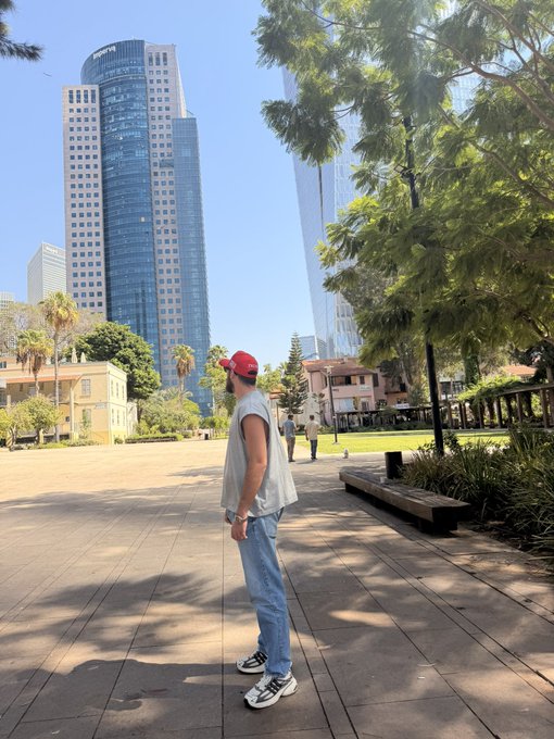 A man in a red cap and gray vest looks up at towering skyscrapers, with "GROWVA" visible on one building—perfect backdrop for a "best caption gets 1 SOL" challenge.